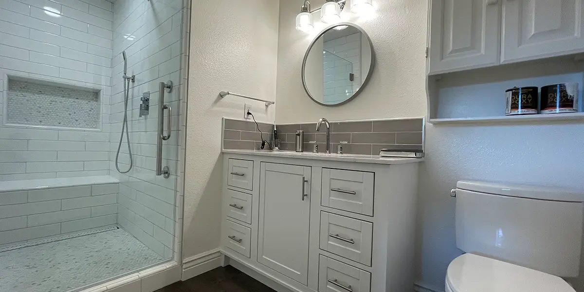 Medium bathroom remodel in California with white vanity, white walk-in shower, and round elegant mirror