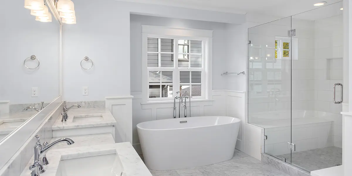 Big white bathroom with marble tile, white freestanding tub, and double sinks