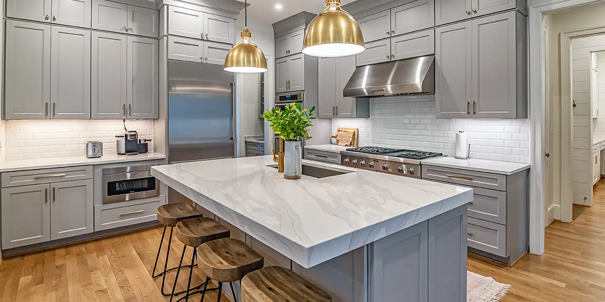 Large open space kitchen with kitchen island, marble countertops, gray cabinets, and golden accessories