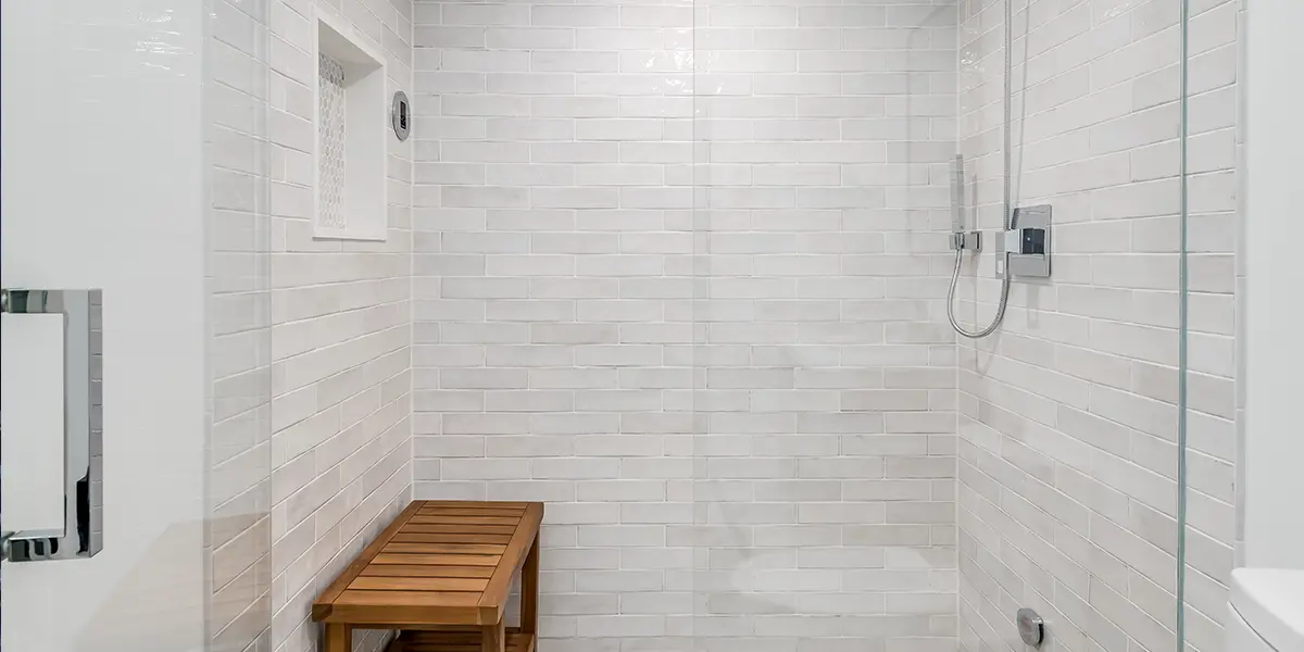 large walk-in shower with wooden bench and marble surround tile