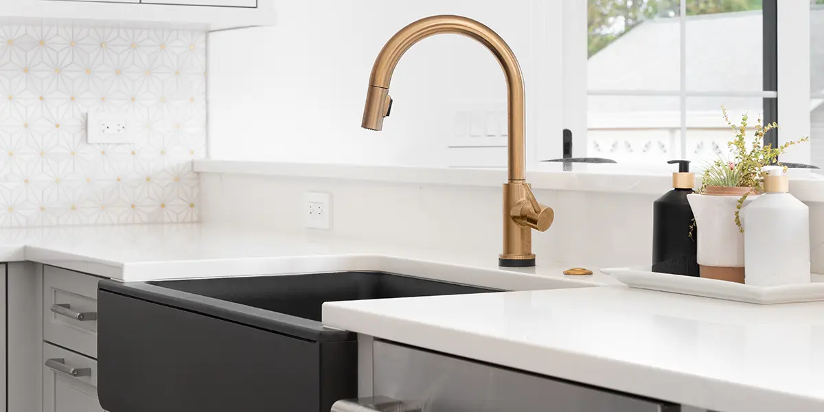 Black matte farmhouse sink with golden faucet and gray cabinets