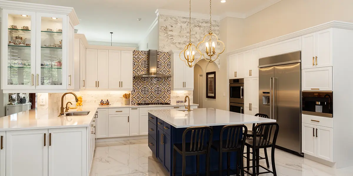 Elegant kitchen with white cabinets and classy navy blue kitchen island with golden lights above it