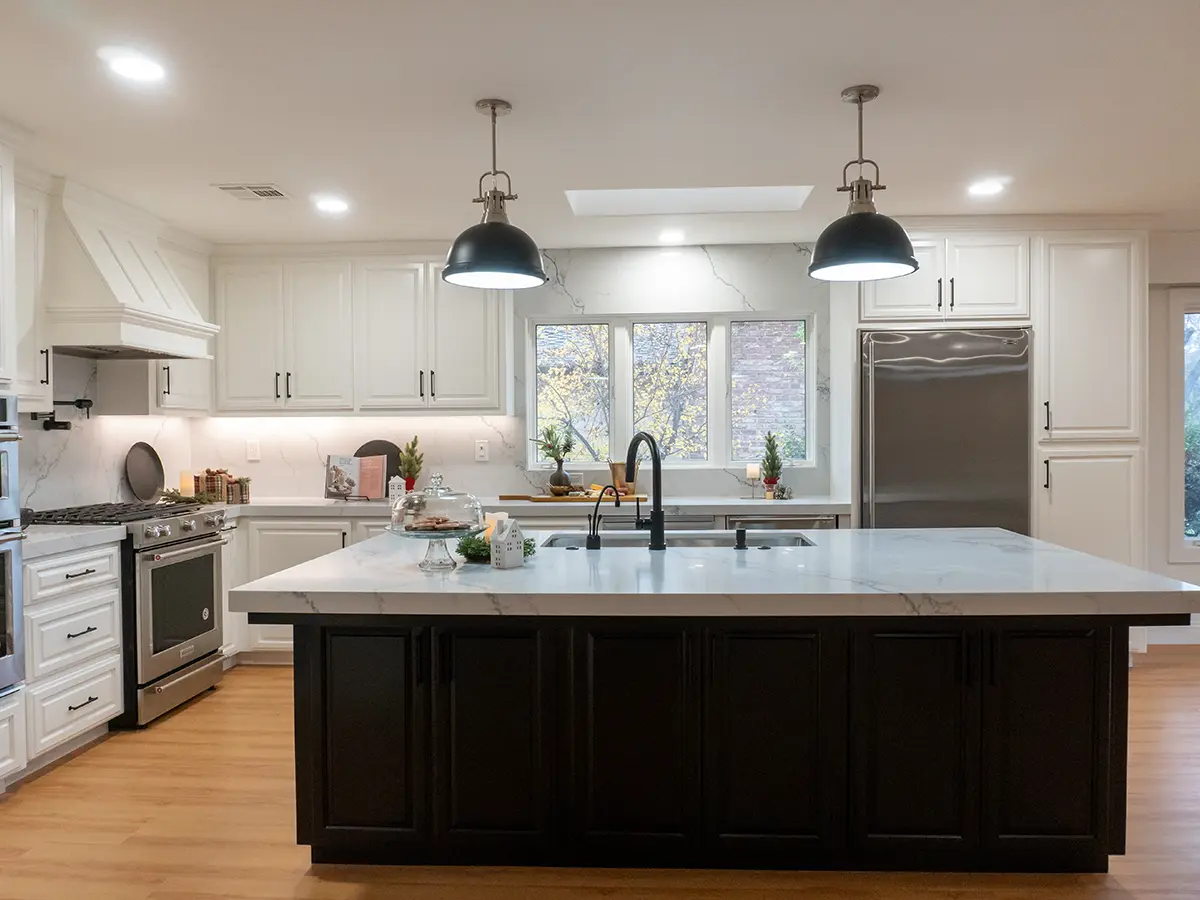 A dark kitchen island with marble countertop and pendant lights