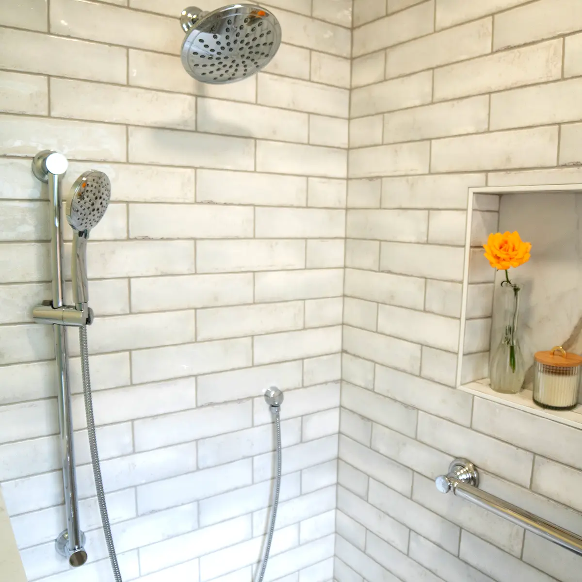 A remodeled shower with white tiling and a vase with an orange flower