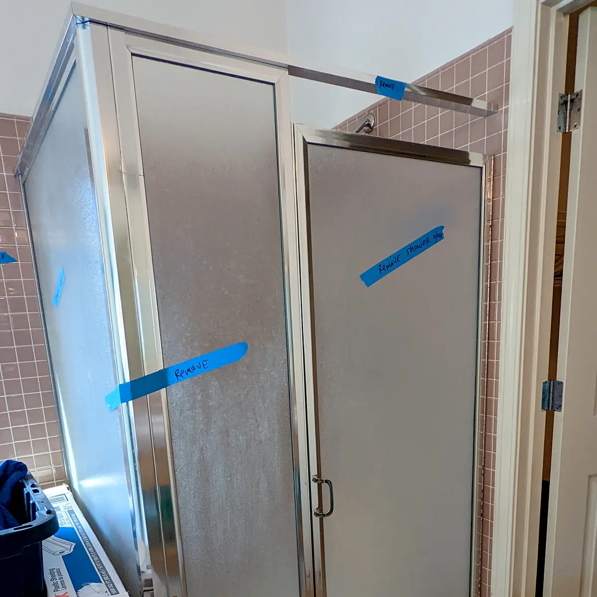 An old glass-shower with blue painter's tape that has different instructions for the builders