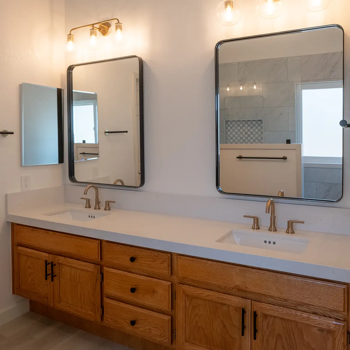 A new bathroom with wood cabinets on a double vanity and large square mirrors