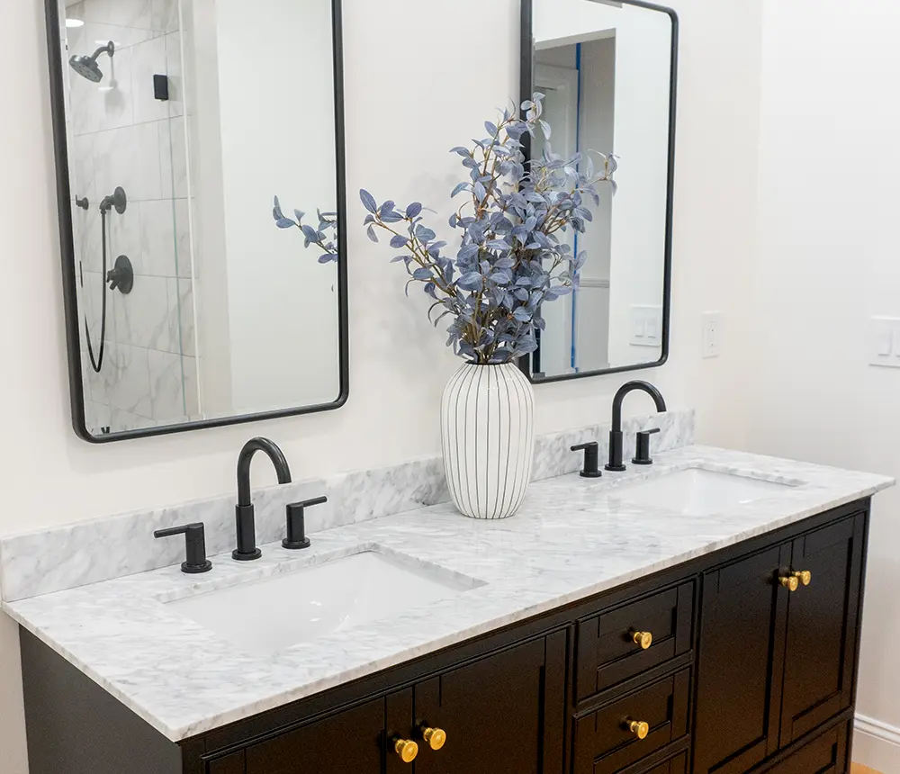 A double vanity with dark cabinets, two square mirrors, and two dark faucets