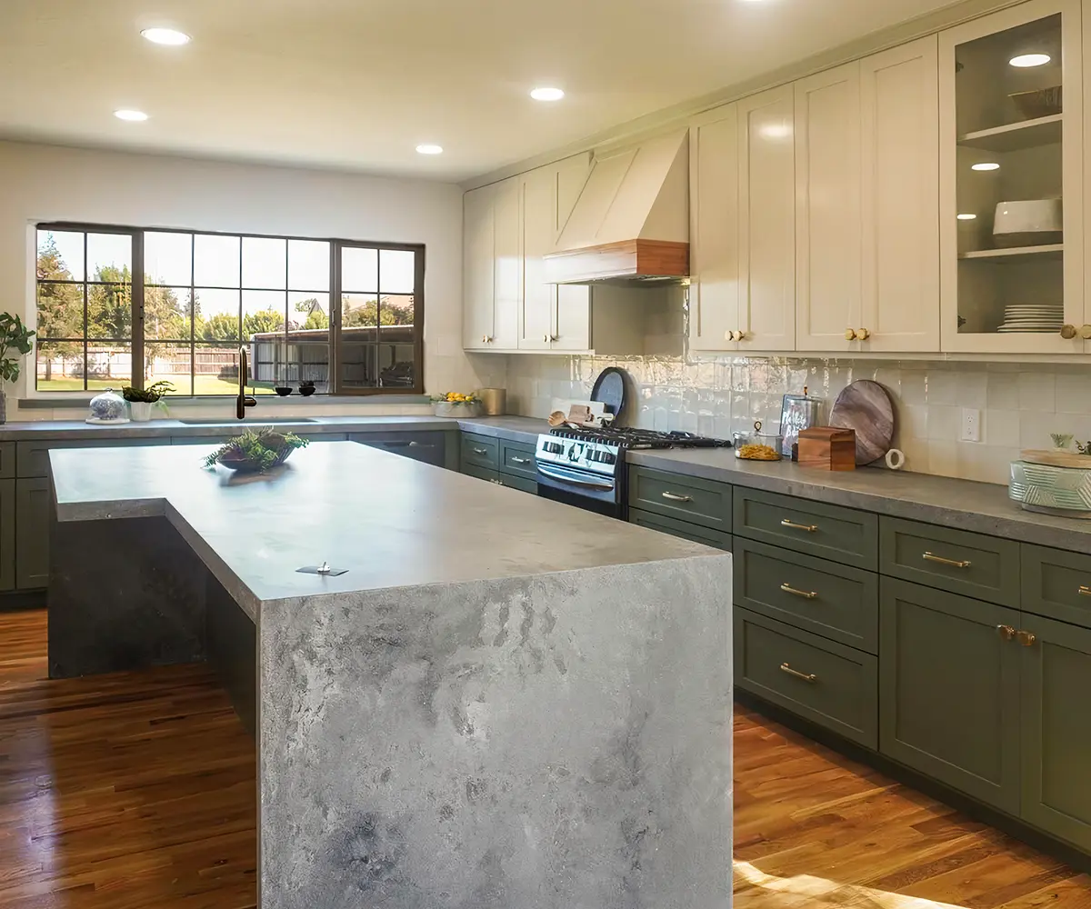 A kitchen with green base cabinets, white upper cabinets, and what looks like a concrete kitchen island