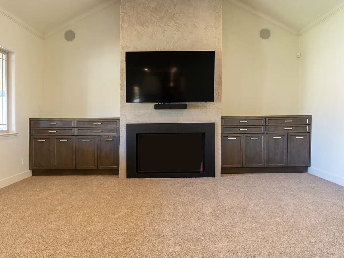 An empty room with two large cabinets, a fireplace, and a TV mounted on the wall