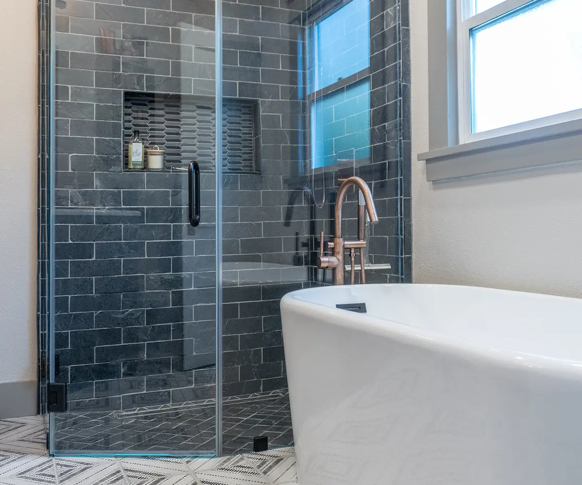A glass walk-in shower with a free standing tub that has a silver faucet
