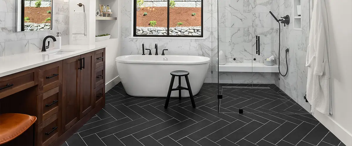 Black tile flooring in a bathroom with white tub and wood vanity