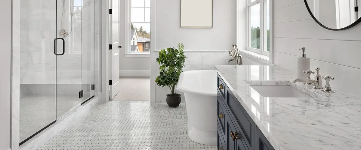 A white bathroom with a dark blue vanity, a tub, and a glass shower