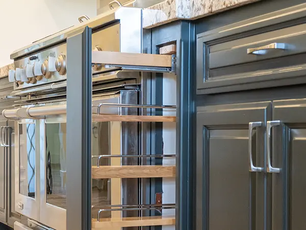 Pull-out spice rack storage beside a professional range in slate blue kitchen cabinets