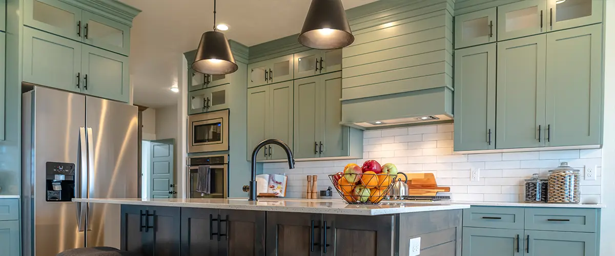 Light green kitchen cabinets in a space with pendant lights