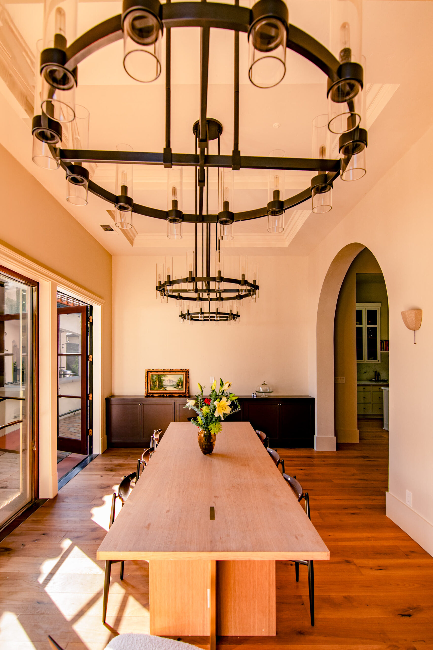 Dining room with twin iron ring chandeliers over a white oak table and an arched doorway