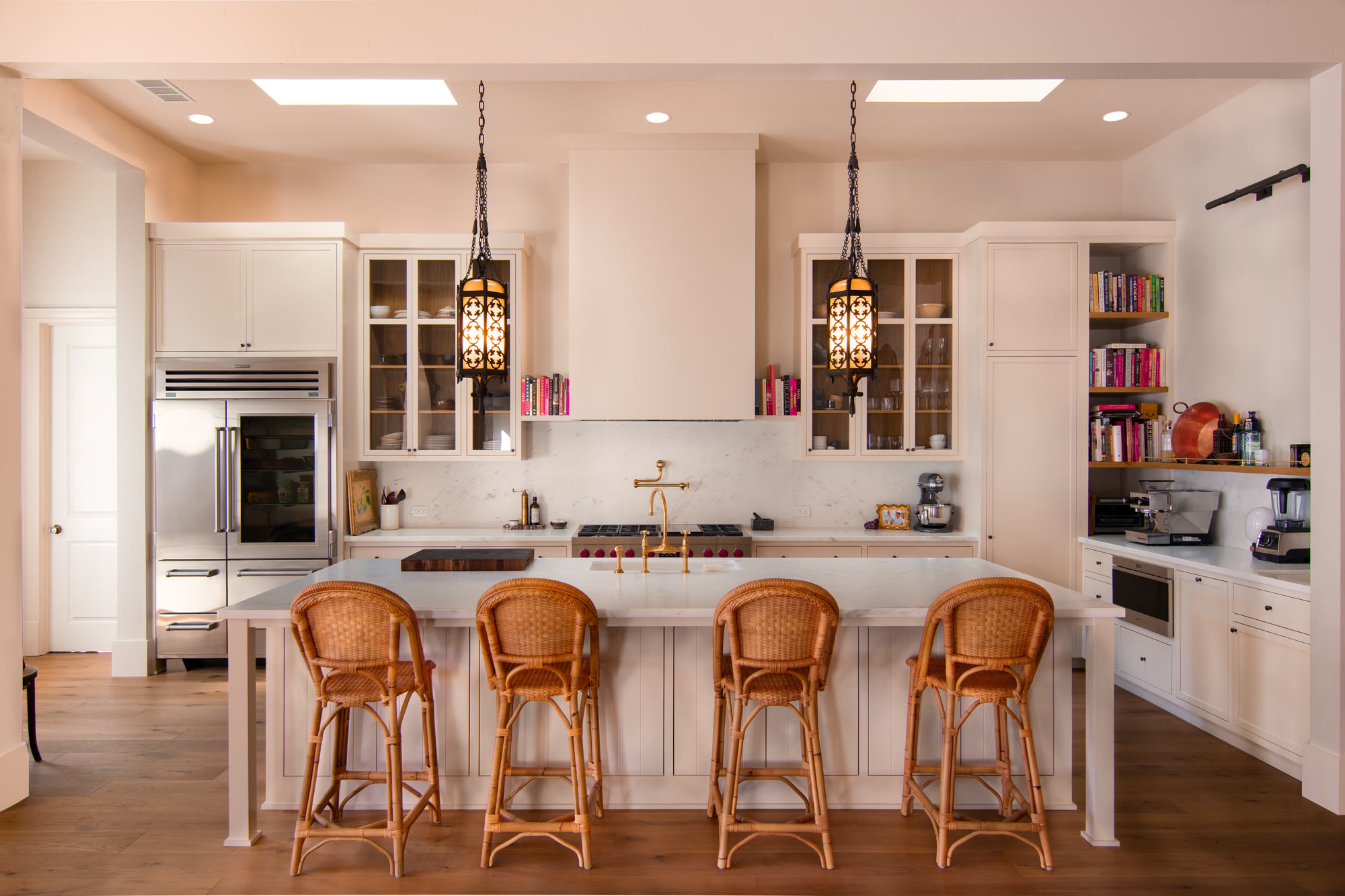 Custom luxury kitchen with a Carrara marble island, rattan stools, and iron lantern pendants