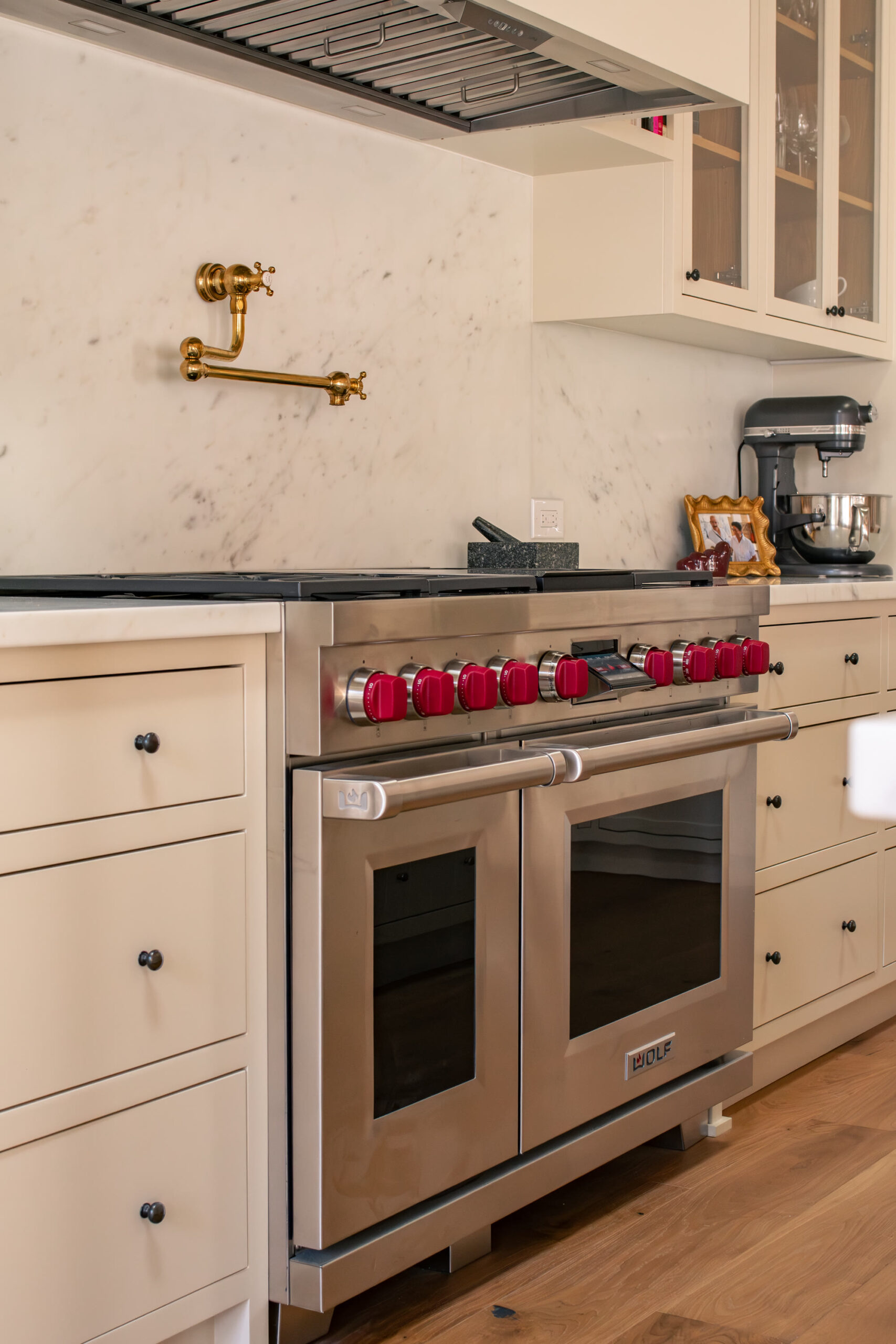 Wolf range with red knobs, a solid-bronze pot filler, and book-matched Carrara backsplash